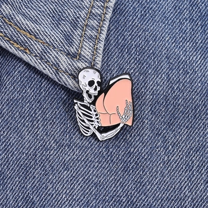 Cartoon skeleton hugging pink butt enamel pin on denim jacket, Halloween style