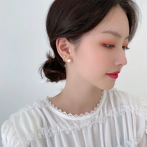 Close-up of pearl stud and golden bead earrings worn by a model in soft lighting