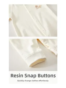 Détail du body bébé avec boutons en résine, poignets côtelés et broderie chiot crème
