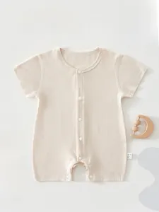 Detailed flat lay of beige infant bodysuit with snap buttons and wooden moon rattle toy