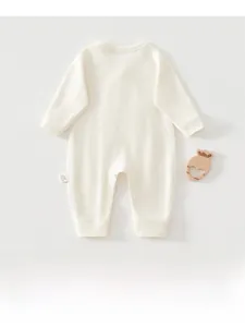 Close-up of a cream newborn cotton romper with heart-shaped wooden teether prop