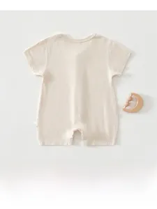 Flat lay of soft cotton baby bodysuit in cream white with a wooden rattle detail