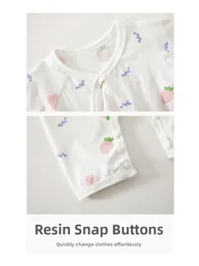 Détail d'un body bébé en coton blanc avec imprimés fraises et boutons-pression en résine