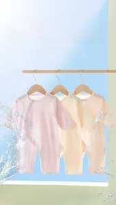 Macro detail of three cotton baby bodysuits in soft pink and beige colors with side buttons