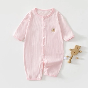 Detail of baby pink ribbed cotton romper with bear embroidery and wooden rattle