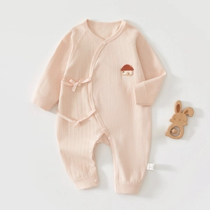 Détail d'une grenouillère bébé en coton rose avec liens et broderie écusson maison
