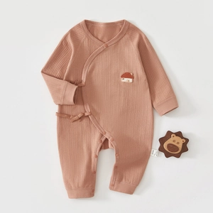 Détail d'un body bébé en coton côtelé rose brique avec broderie maison et nœuds latéraux