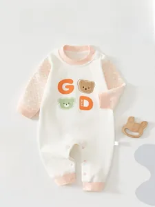 Close-up of baby romper showing soft ivory cotton fabric, pink ribbed cuffs and snap button crotch