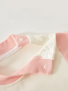 Detailed view of shoulder snap design on pink and white cotton infant romper