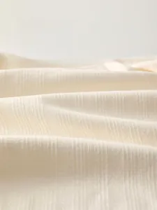 Detail view of cream fine cotton fabric with vertical stripe texture and soft breathable feel