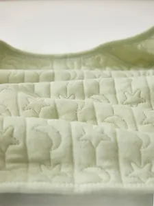 Macro shot of light green quilted baby fabric with moon and star stitching patterns
