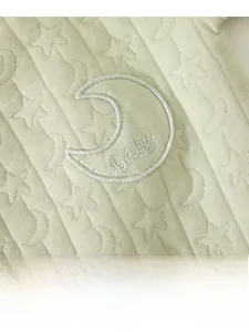 Detail of baby romper featuring light green jacquard fabric with embroidered moon patch