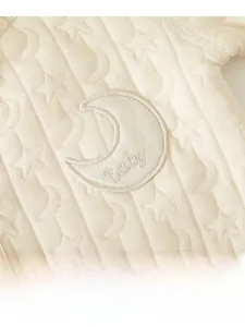 Detail of baby onesie featuring quilted star and moon jacquard fabric with moon patch