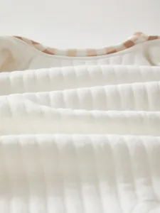 Detailed close-up of soft ribbed cotton baby jumpsuit fabric with check pattern piping