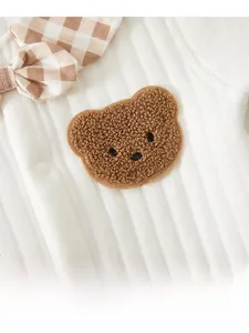 Detailed macro view of baby romper featuring a plush bear patch and checkered bow tie