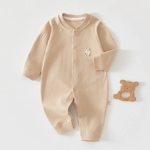 Dettaglio di una tutina per neonati in cotone a coste beige con ricamo di un orsetto