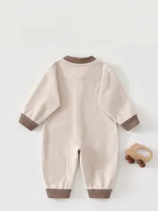 Detailed back view of a beige ribbed newborn romper with brown trim and wooden toy decor