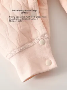 Détail de boutons-pression en résine sur tissu matelassé rose de barboteuse pour bébé