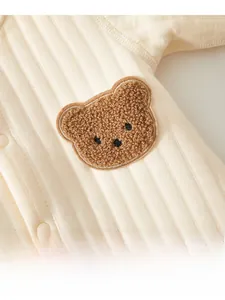 Détail d'une grenouillère matelassée beige pour bébé avec broderie d'ours en peluche 3D