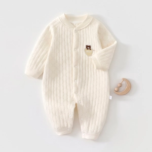 Detailed quilted texture of cream newborn romper with bear pattern and wooden rattle
