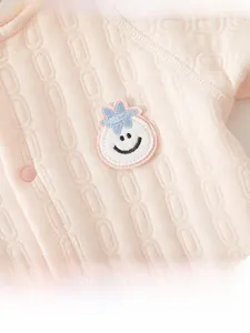 Detail of pink baby romper with jacquard knit texture, smiley embroidery, and resin snaps