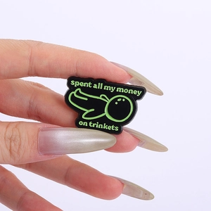 Detalle de una mano sosteniendo un pin de esmalte negro con texto en verde fluorescente