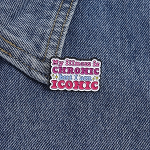Close-up of enamel quote pin on denim jacket with colorful My illness is chronic but I am iconic