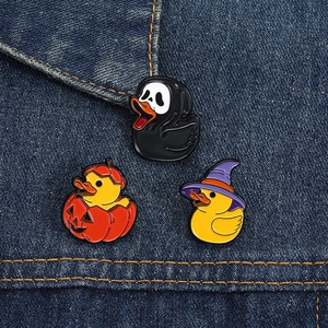 Detailed close-up of three Halloween duck enamel pins on dark blue denim fabric texture