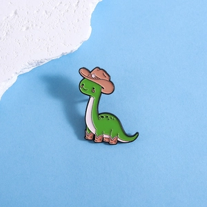 Detail of green cartoon dinosaur enamel pin with a cowboy hat on a blue background