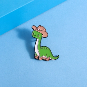 Detail of green dinosaur enamel pin wearing a brown cowboy hat and boots on blue background