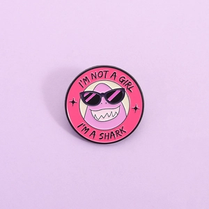 Rosa Emaille-Hai-Anstecknadel mit Text 'I'M NOT A GIRL I'M A SHARK' auf lila Hintergrund