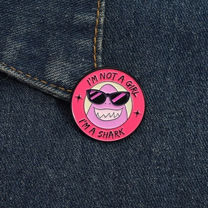 Makro-Detail einer runden rosa Emaille-Anstecknadel mit Hai-Motiv auf blauem Denim-Stoff