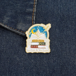 Metal enamel book brooch featuring mountains and stars on denim background