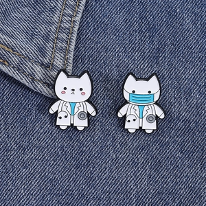 Detailed view of two cartoon cat doctor enamel pins on blue denim fabric texture