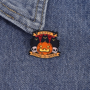 Detailed view of Halloween cat and pumpkin enamel pin on denim fabric background