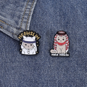 Detail of Meowslim and Hala Habibi cat enamel pins pinned on dark blue denim fabric