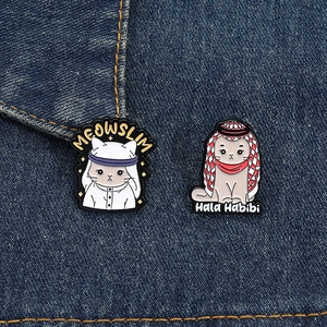 Detailed close-up of cute cat enamel pins featuring Meowslim and Hala Habibi designs on denim