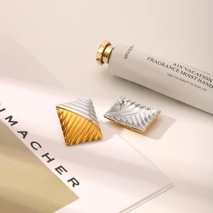 Detail of mixed-tone rectangular stud earrings with textured ripple design on magazine