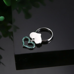 Bague argentée avec double pendentif cœur et pierres de zircon vert sur fond noir élégant