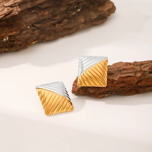 Detailed view of square two-tone geometric earrings with diagonal texture on wood