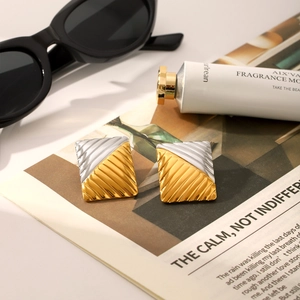 Macro detail of geometric two-tone gold and silver earrings with textured ribbed surface