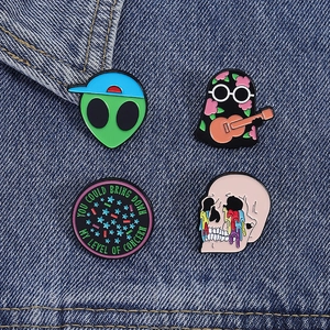 Set of four unique enamel pins with alien, ghost, skull, and slogan on denim fabric