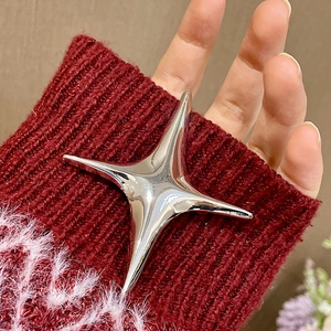 Detail einer silbernen Sternbrosche an einem dunkelroten Strickärmel mit Metallstruktur