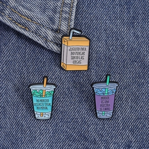 Three-piece enamel pins set with juice box and soda designs on blue denim fabric