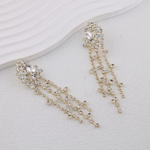 Detail shot of long golden tassel earrings with pear-shaped rhinestones on white decor