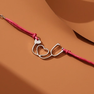 Detail of pink woven bracelet with silver heart stethoscope charm on textured backdrop