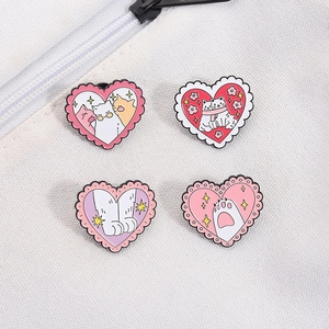 Détail de badges en émail en forme de cœur avec chats roses sur un tissu blanc