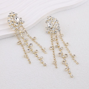 Macro detail of gold-plated tassel earrings with sparkling cubic zirconia on a white wave