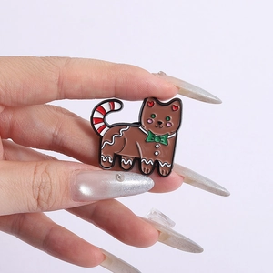 Close-up of a gingerbread cat enamel pin with a green bow and red striped tail
