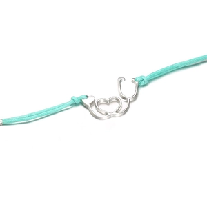 Close-up of mint green woven bracelet with silver heart stethoscope charm on white backdrop